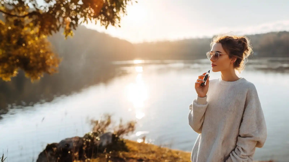 Une vapoteuse avec une cigarette électronique debout au bord d'un lac