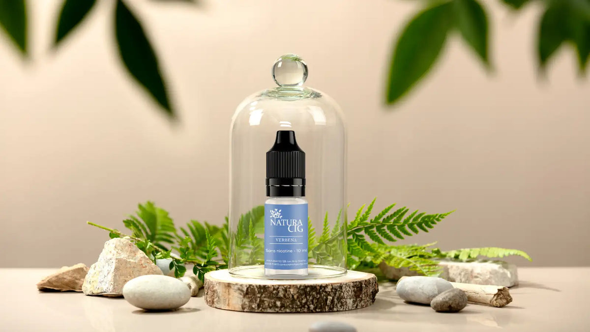 Flacon de e-liquide Naturacig sous une cloche en verre sur un rondin de bois entouré d’éléments naturels