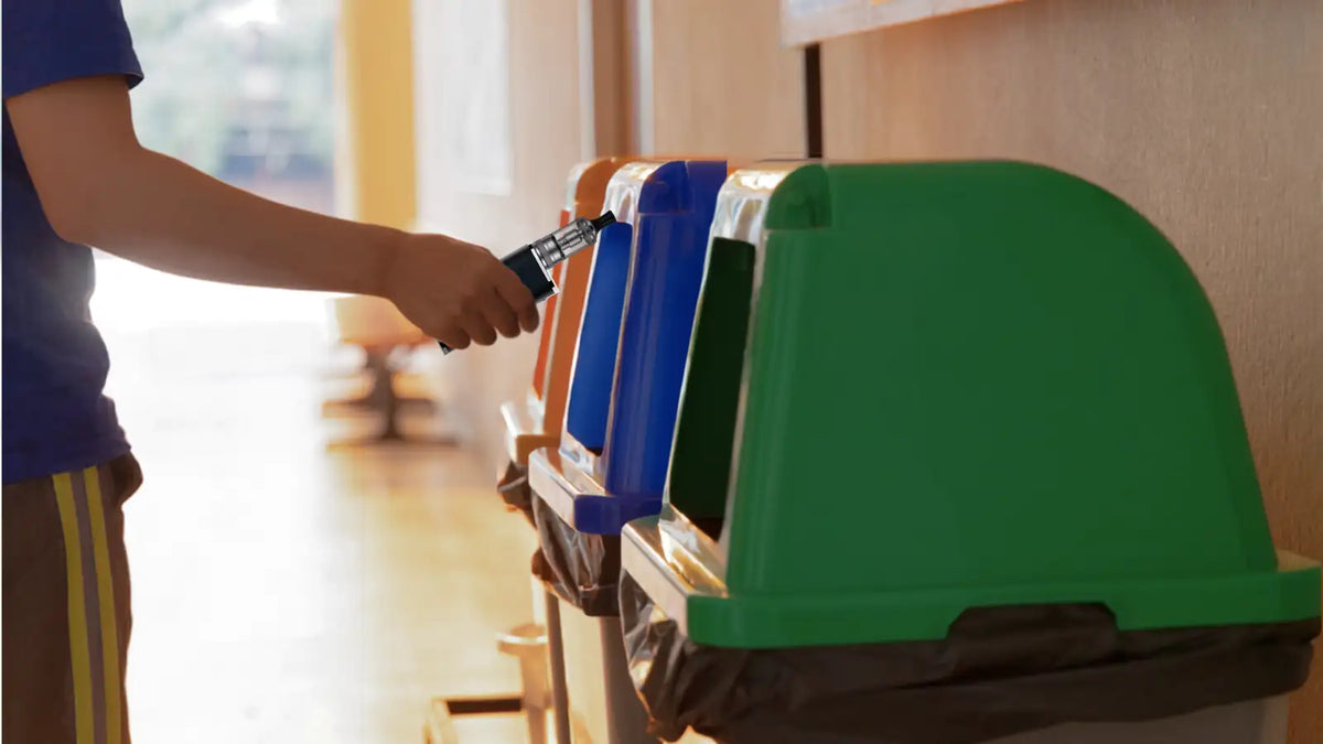 Une personne avec une cigarette électronique dans la main devant des poubelles de recyclage