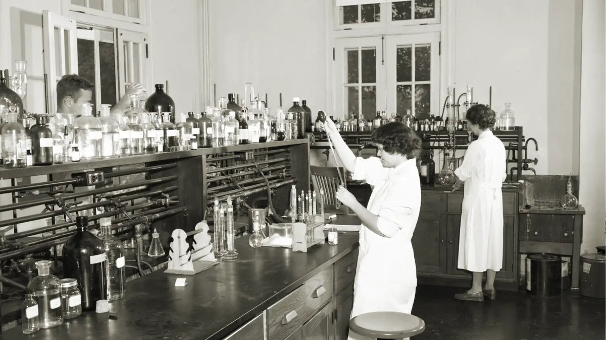 Un laboratoire de chimie ancien en noir et blanc avec des laborantines en train de réaliser des mélanges de liquides