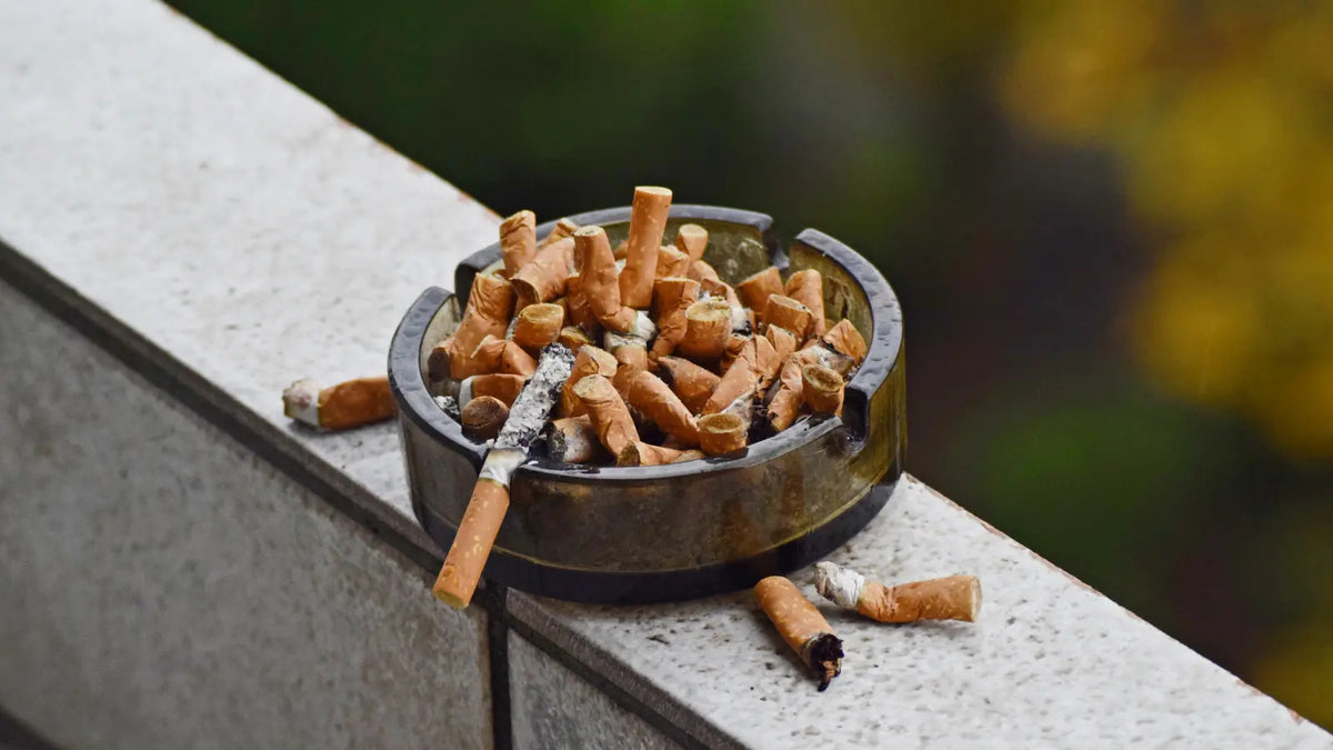 Cendrier rempli de cigarettes écrasées et une cigarette se consume sur le rebord