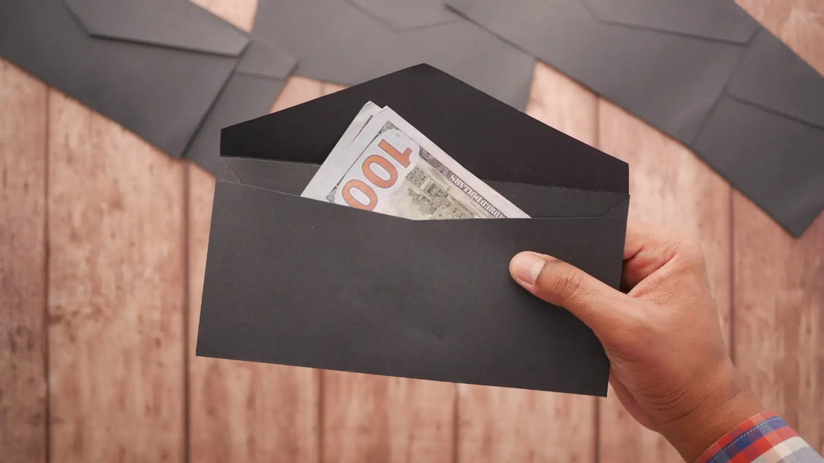 Dans une main une enveloppe noire ouverte avec des billets de banque à l'intérieur