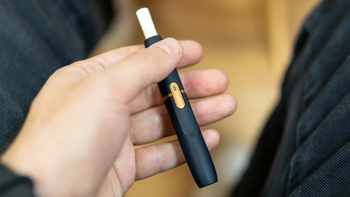 Une e-cigarette comprenant une cartouche de tabac à chauffer tenu dans une main